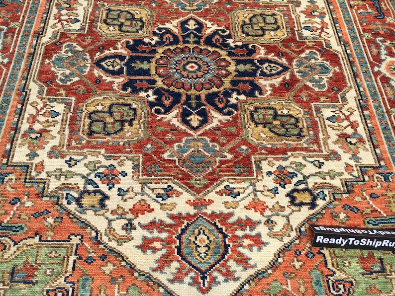 May include: A detailed close-up of a Persian-style rug with a central medallion design. The rug features a complex pattern in shades of red, navy, cream, and green. The intricate design includes floral and geometric elements, creating a rich, textured appearance.