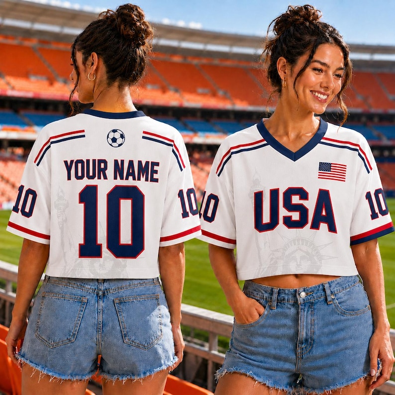 Two women wearing white soccer jerseys with the text "YOUR NAME 10" and "USA" printed on them, standing in front of a stadium.
