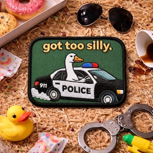 May include: A green patch with the text "got too silly." features a goose driving a police car. The car is black and white with the word "POLICE" on the side. Other items include sunglasses, donuts, a rubber duck, and handcuffs.