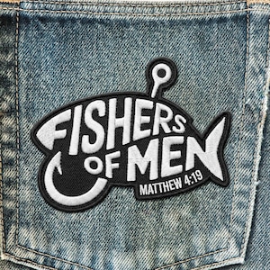 May include: A black and white embroidered patch in the shape of a fish, with the words "FISHERS OF MEN" and "MATTHEW 4:19" in white lettering. The patch is sewn onto a blue denim fabric.