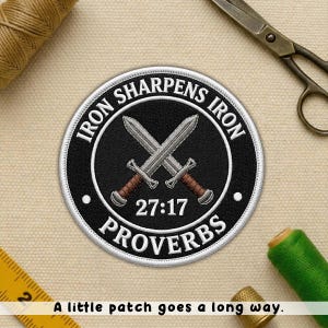 May include: Embroidered patch with the text "IRON SHARPENS IRON" and "PROVERBS 27:17" surrounding two crossed swords. The patch is black with white and brown accents. A sewing kit and scissors are in the background.