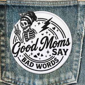 May include: A white circular patch with black embroidered text and a skeleton illustration. The text reads "Good Moms Say Bad Words". The skeleton is wearing a headband and giving a peace sign. A lightning bolt and stars are also featured.