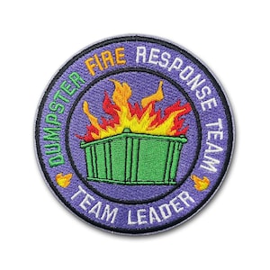 May include: Embroidered patch with a purple background and a green dumpster on fire. The patch reads "Dumpster Fire Response Team Team Leader" in a circular design with yellow and white text.