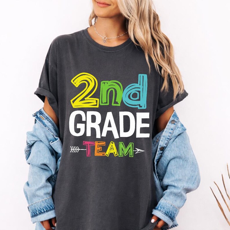May include: Dark gray t-shirt with the words "2nd GRADE TEAM" in colorful block letters. The "2nd" is yellow and green, "GRADE" is white, and "TEAM" is multi-colored with an arrow design.