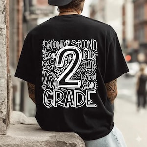 May include: Black t-shirt with a white graphic design. The design features the number "2" with the words "SECOND" and "GRADE" in a handwritten style. The shirt is a casual style.