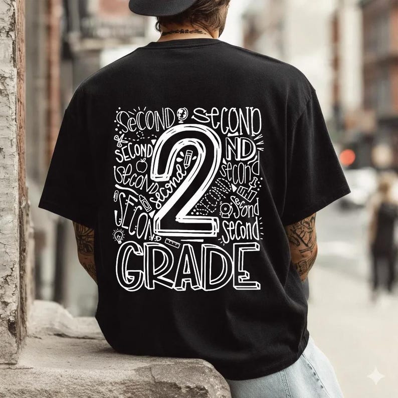 May include: Black t-shirt with a white graphic design. The design features the number "2" with the words "SECOND" and "GRADE" in a handwritten style. The shirt is a casual style.