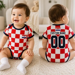 May include: A baby bodysuit featuring a red and white checkered pattern with dark blue trim. The front displays a small Croatian flag emblem. The back shows the Croatian flag, the text CUSTOM NAME, and the number 00 in dark blue block lettering.