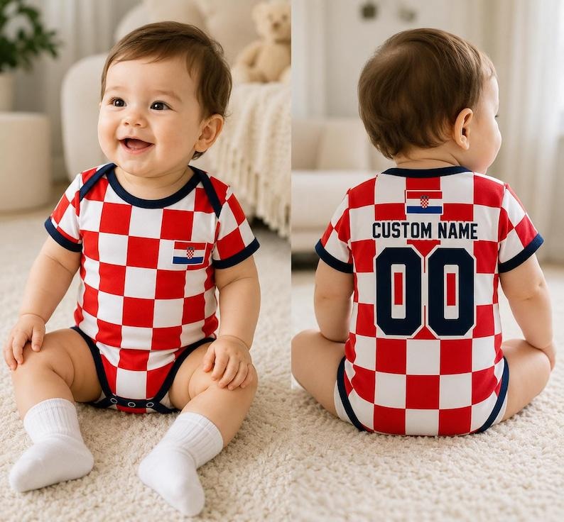 May include: A baby bodysuit featuring a red and white checkered pattern with dark blue trim. The front displays a small Croatian flag emblem. The back shows the Croatian flag, the text CUSTOM NAME, and the number 00 in dark blue block lettering.