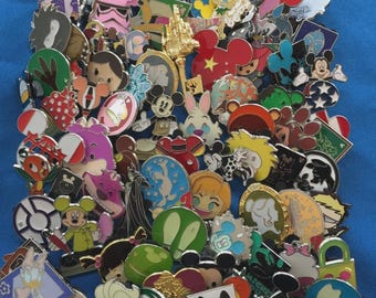 May include: A collection of colorful enamel pins featuring various Disney characters and icons. The pins showcase Mickey Mouse, Minnie Mouse, and other beloved characters, with a variety of shapes and designs. The pins are set against a blue background.