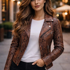 Könnte beinhalten: Braune Lederjacke mit Schlangenmuster, Reißverschluss und silbernen Details. Sie wird über einem weißen T-Shirt und mit schwarzen Jeans getragen. Die Person hat lange, wellige, braune Haare.