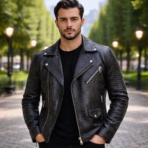 Puede incluir: Chaqueta de cuero negra con textura de piel de serpiente. La chaqueta tiene un estilo motero clásico con cuello de solapa, cremallera asimétrica y múltiples bolsillos. El modelo lleva una camiseta negra y pantalones negros.