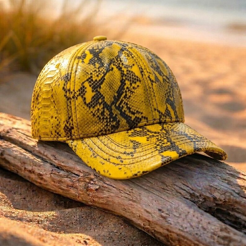 May include: A baseball cap featuring a vibrant yellow and black snakeskin pattern. The cap has a structured six-panel crown with a curved brim, showcasing a detailed reptilian scale texture across the entire surface of the headwear.