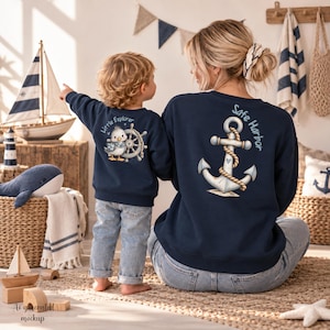 Könnte beinhalten: Ein marineblaues Sweatshirt für Kinder mit einem Entenmotiv, einem Steuerrad und dem Text Little Explorer sowie ein passendes marineblaues Sweatshirt für Erwachsene mit einem großen Anker-Motiv, Seil und dem Text Safe Harbor.