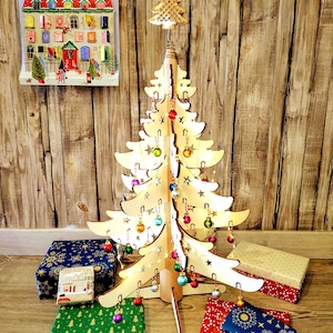 May include: A wooden Christmas tree with star-shaped cutouts and small, colorful ornaments. The tree is illuminated with lights and topped with a gold star. Several wrapped gift boxes in various patterns and colors are at the base of the tree. A Christmas advent calendar is on the wall.