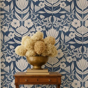 Puede incluir: Una mesa auxiliar de madera con un cajón y un cuenco de latón lleno de flores secas. La mesa está colocada contra un papel pintado floral azul. La habitación tiene un estilo clásico y elegante.