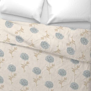 May include: A cream-colored duvet cover and pillowcases with a repeating pattern of blue floral blooms and tan stems. The bedding is arranged on a white bed, creating a soft and inviting aesthetic.