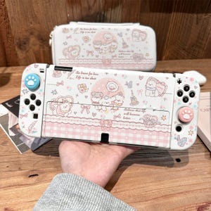 May include: A white gaming console case and matching protective shell featuring a pastel pink and blue pattern of cartoon dogs, hearts, bows, and butterflies. The design includes the text Be brave for love, Life is too short, and Believe that life will become better. Includes blue and pink paw print thumb grips.