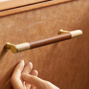 Op de afbeelding: Close-up van een houten nachtkastje met een bruine leren lade en een donkerbruine en gouden handgreep. Bovenop ligt een boek met de titel "RADIO ASTRONOMER". De handgreep is ongeveer 15 cm lang.