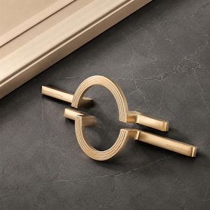 May include: Two brushed gold cabinet pulls featuring a semi-circular design with concentric grooved lines. Each handle has a straight arm extending from the arc, with the text Mason Robinson engraved on the flat surface of the metal hardware.