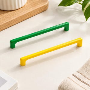 May include: Two long, slender cabinet pulls, one in a vibrant green and one in a bright yellow, each featuring a smooth, cylindrical bar design with rounded ends and the text Mason Robinson printed in small white letters on the top surface.