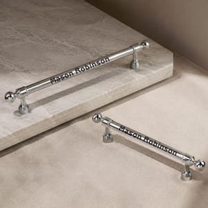 May include: Two polished chrome cabinet pulls with spherical ends and cylindrical bars. Each handle features the black engraved text Mason Robinson centred along the length of the metal bar, showcasing a reflective finish and a classic hardware design.