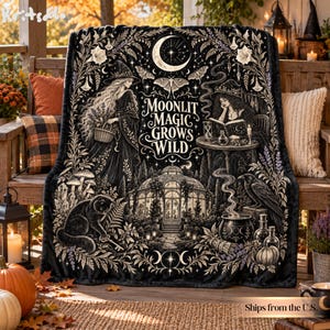 Puede incluir: Una manta de color negro y blanco con una ilustración detallada de dos figuras con sombreros de bruja, un invernadero, un gato, un cuervo y un caldero. El texto "MOONLIT MAGIC GROWS WILD" está centrado y rodeado de motivos botánicos.