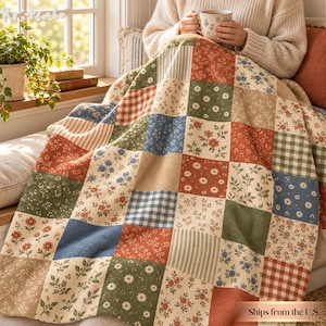 May include: A patchwork quilt featuring a variety of square fabric panels in shades of red, blue, green, and beige. The patterns include floral prints, gingham checks, and thin stripes. The quilt is draped over a surface, displaying a mix of textures.