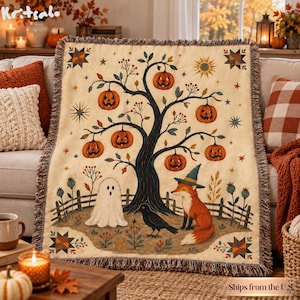 May include: A woven throw blanket featuring a cream background with a central dark tree bearing orange jack-o'-lanterns. Below the tree, a white ghost, a black crow, and an orange fox wearing a blue witch hat stand near a wooden fence.