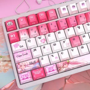 Può includere: Una tastiera meccanica personalizzata con tasti rosa e bianchi. I tasti presentano illustrazioni e testo in stile anime, tra cui "Shift", "Ctrl" e "Win". La tastiera ha una combinazione di colori rosa e bianco, con una base rosa abbinata.
