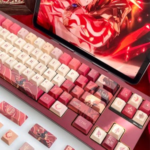 May include: A custom mechanical keyboard with a red and white color scheme. The keycaps feature various designs and text, including "SHIFT" and "CTRL". The keyboard is displayed with a tablet showing a red graphic.