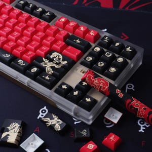 May include: A custom mechanical keyboard with red and black keycaps. The keycaps feature various symbols and designs, including a dragon and other graphics. The keyboard has a clear case and a matching wrist rest.