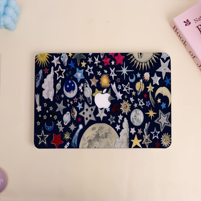 Peut inclure: Une peau d'ordinateur portable bleu marine avec un motif c&eacute;leste. Elle pr&eacute;sente des &eacute;toiles, des lunes, des plan&egrave;tes et des soleils de diff&eacute;rentes couleurs. Le logo Apple est blanc. Motif fantaisiste sur le th&egrave;me de l'espace.