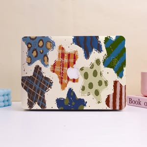 May include: A laptop case featuring a cream background with colorful star shapes in various patterns, including plaid, stripes, and polka dots. The case has a cutout for the Apple logo.