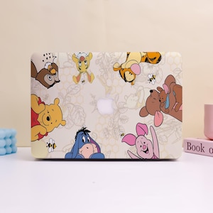 Może przedstawiać: Etui na laptopa z fantazyjnym wzorem z postaciami Kubusia Puchatka. Etui prezentuje ilustracje Kubusia, Tygryska, Prosiaczka, Kłapouchego i Sowy, na jasnobeżowym tle z kwiatowym wzorem. Widoczne jest logo Apple.