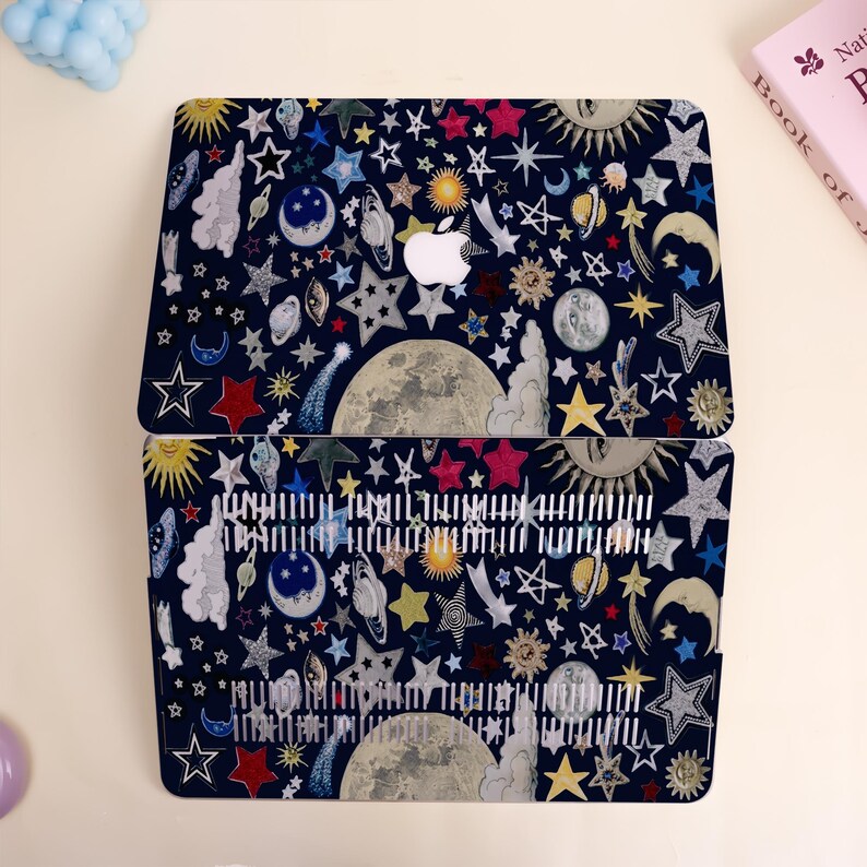 Peut inclure: Une coque d'ordinateur portable bleu fonc&eacute; avec un motif c&eacute;leste compos&eacute; d'&eacute;toiles, de lunes, de soleils et de plan&egrave;tes de diff&eacute;rentes couleurs. Le logo Apple est visible. Le motif est r&eacute;p&eacute;t&eacute; sur la moiti&eacute; inf&eacute;rieure de l'ordinateur portable.