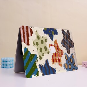 May include: Laptop case with a cream background and colorful star-shaped designs. The stars feature various patterns, including stripes, polka dots, and plaid, in shades of blue, green, orange, and brown. The case is open, revealing the laptop's screen.