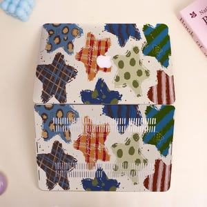 May include: A laptop case with a colorful star pattern. The design features stars in various styles, including plaid, polka dots, and stripes, in shades of brown, orange, blue, and green. The case has a white background with a few small dots.