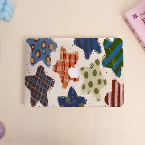 May include: A laptop skin featuring a pattern of colorful star shapes in various designs, including plaid, polka dots, and stripes. The stars are in shades of blue, brown, green, and orange, with a white Apple logo visible.