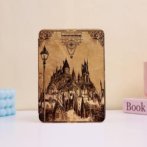 May include: A rectangular wooden tablet featuring a detailed laser-engraved illustration of a castle on a hill overlooking a village. The design includes a street lamp, a compass motif at the top with the text Tu Camino Sigue, and ornate borders.