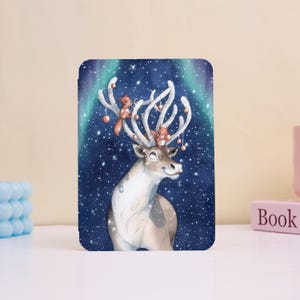 May include: A rectangular, illustrated design featuring a reindeer with large antlers adorned with ornaments and squirrels. The background is a dark blue with falling snow and a green and blue aurora borealis effect.
