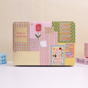 Peut inclure: Une coque rigide pour ordinateur portable présentant un collage de motifs aux tons pastel et de textes inspirants. Les designs incluent un carré à carreaux verts avec 'today is a good day', une section à rayures roses et divers motifs floraux.