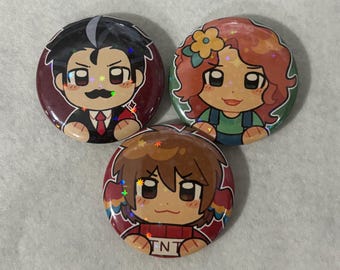 May include: Three circular pin-back buttons featuring colorful anime-style character illustrations with a holographic star finish. One button shows a person with a mustache in a suit, another a person with curly hair and a flower, and one with the text TNT.