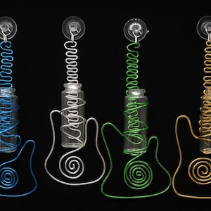 May include: Four decorative guitar-shaped wire art pieces in blue, silver, green, and gold. Each piece features a small glass bottle wrapped in wire, with a suction cup at the top. The guitar bodies have a spiral design.