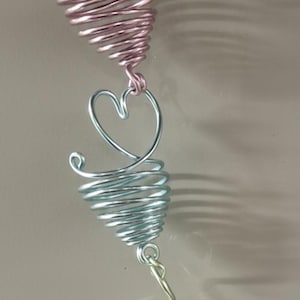 May include: A decorative hanging ornament featuring a series of spiraled wire cones and heart-shaped accents in shades of pink, blue, and green. The ornament is suspended from a clear suction cup.