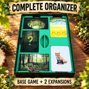 Könnte beinhalten: Eine grüne Brettspiel-Organizer-Box mit vier Kartenfächern. Die Karten zeigen Illustrationen eines Waldes, eines Fragezeichens, einer Berglandschaft mit drei Sternen und eines Fuchses. Der Text COMPLETE ORGANIZER und BASE GAME + 2 EXPANSIONS ist sichtbar.