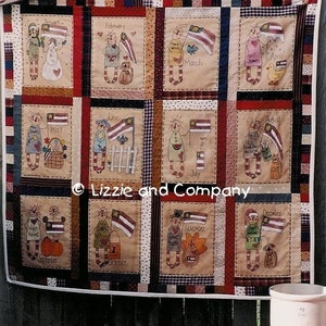 May include: A patriotic quilt with a patchwork design featuring a different illustration for each month of the year. Each illustration includes a person holding a small American flag. The quilt is hanging on a wooden fence with a sign that reads "USA USA".