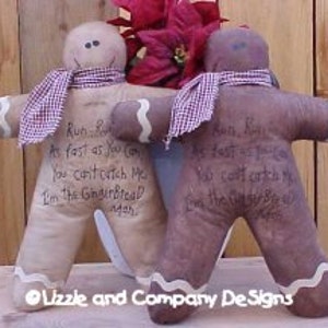 Op de afbeelding: Twee gingerbread man poppen met rood-wit geblokte sjaals. De poppen zijn gemaakt van stof en hebben een bruin en beige kleurenschema. De poppen hebben de tekst "Run, Run as fast as you can You can't catch me I'm the Gingerbread Man" erop geschreven.