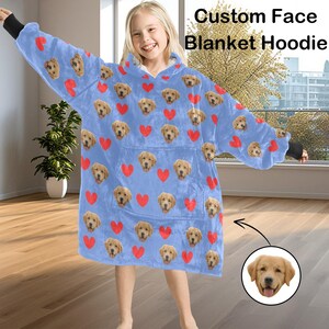 Pu&ograve; includere: Una felpa con cappuccio a coperta azzurra con un motivo ripetuto di facce di cane e cuori rossi. La felpa con cappuccio ha un'ampia tasca frontale e polsini neri. Il testo sull'immagine recita "Custom Face Blanket Hoodie."