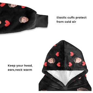Pu&ograve; includere: Coperta con cappuccio nera con interno bianco, decorata con cuori rossi e volti. Il testo "Keep your head, ears, neck warm" e "Elastic cuffs protect from cold air" sono visibili.