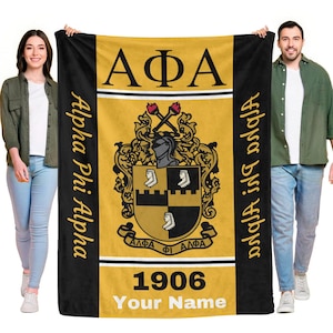 May include: A black, gold, and white blanket featuring the Greek letters ΑΦΑ, a crest, and the year 1906. The words "Alpha Phi Alpha" are printed vertically on the left side, and "Alpha Phi Alpha" is printed vertically on the right side.